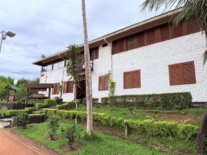 Fachada exterior del 'Hotel Waira Selva' en Puerto Nariño, un edificio blanco de dos pisos con ventanas de madera marrón y jardines al frente.