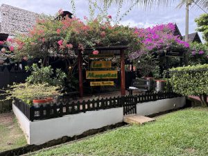 Detalle de la fachada del Restaurante Las Margaritas, destacando su jardín ornamental con flores tropicales y techo de paja tradicional al fondo. La entrada presenta un estilo rústico con madera oscura y señalización colorida.