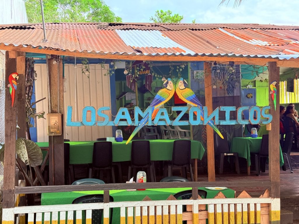 Decoración temática del Restaurante Los Amazónicos. La imagen resalta el trabajo artesanal en madera, figuras de aves exóticas y un ambiente de comedor típico bajo un techo de zinc, ideal para turismo gastronómico.