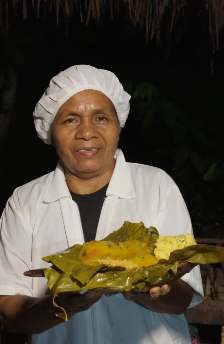 Cocinera presentando un platillo típico regional envuelto en hojas de bijao o plátano, destacando ingredientes amarillos y texturas tradicionales de la cocina artesanal.